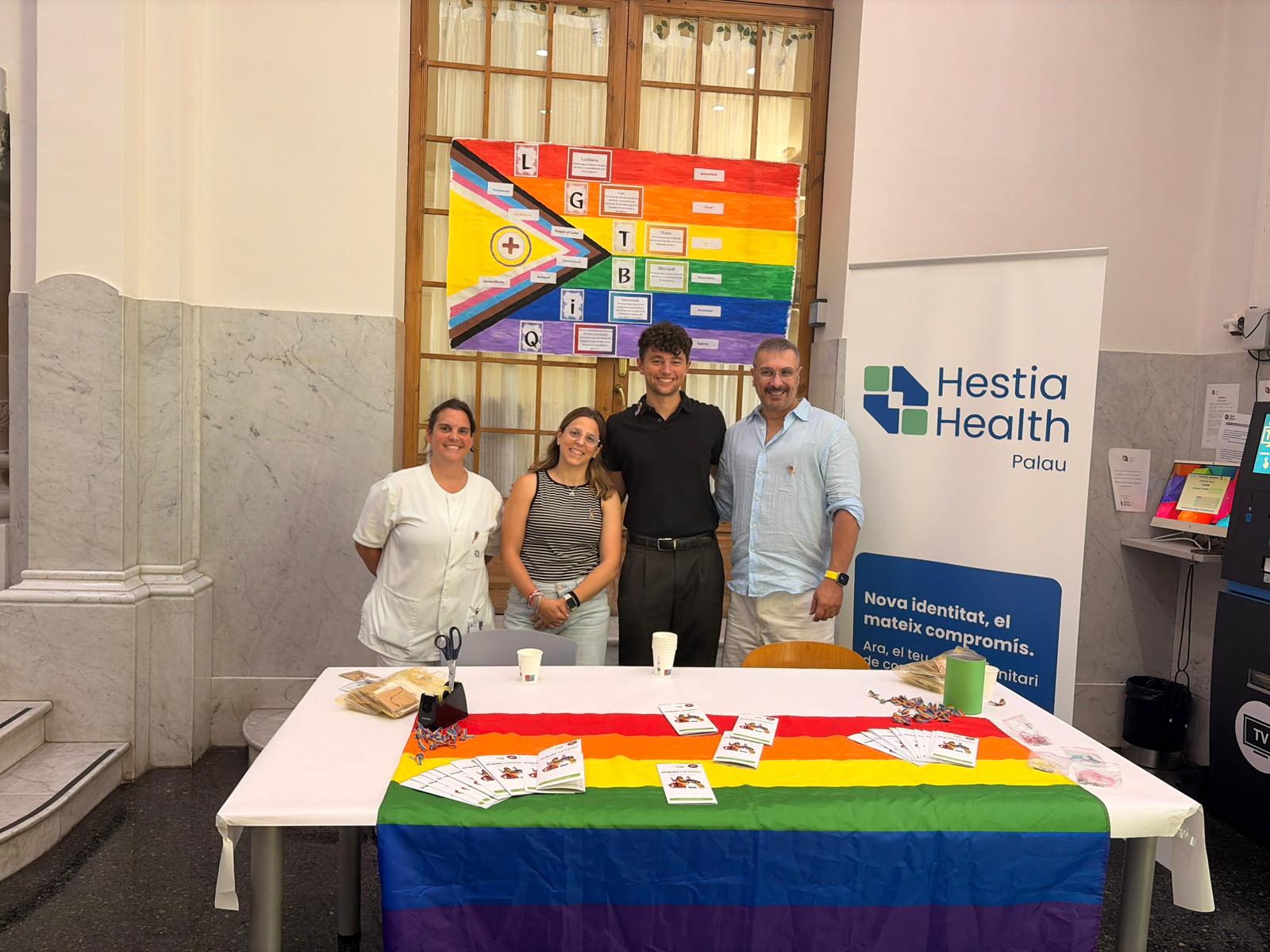 Voluntarios de Generación o2 y profesionales de Hestia Health Palau en la mesa informativa del 28J junto a la bandera Progress